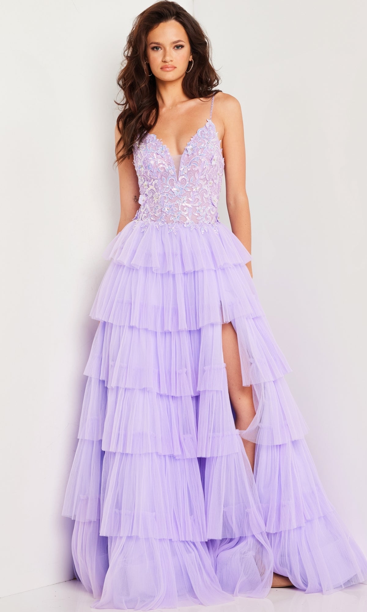 A woman wearing the Jovani Long Prom Dress 37190 with a ruffled tulle skirt, lace embellished bodice, deep V-neckline, and high leg slit stands against a plain white background.